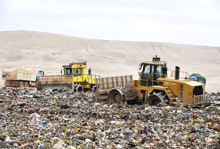 Three vehicles (bulldozers and trucks) surrounded by solid waste at Ghabawi landfill in Jordan.